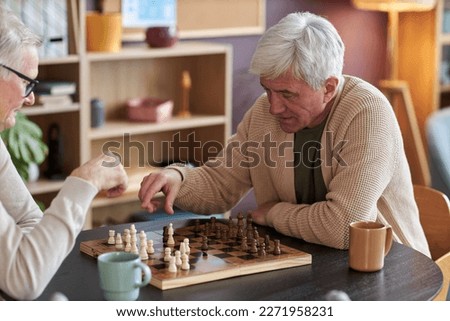 Portrait of white haired senior man playing chess at table in retirement home