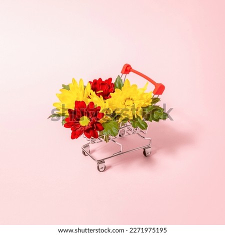 Creative composition with shopping cart full of colorful flowers and leaves against bright pastel pink. Spring discount concept.