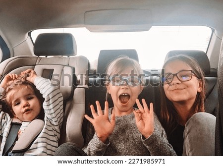 Three cute sisters of different ages are riding in the back seat of a car. Girls scream, indulge and laugh. Road trip with three children. Kids having fun in the automobile. Free space for the text. Royalty-Free Stock Photo #2271985971