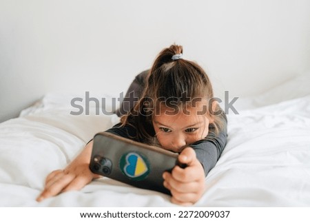 preschool age girl watching cartoons on smartphone on white bedding. 