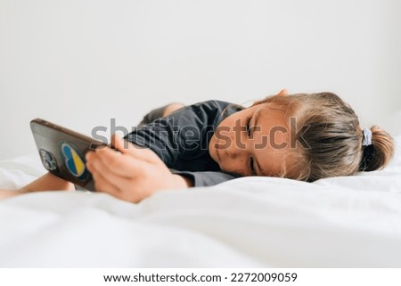 preschool age girl watching cartoons on smartphone on white bedding. 