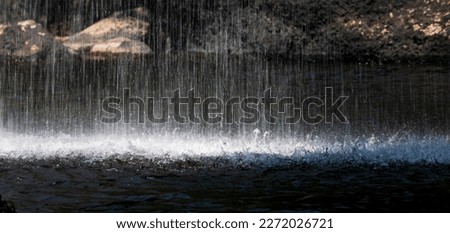 Long speed shutter technique of splashing waterfall drop on pond with dark cave inside asian tropical rainforest in summer.