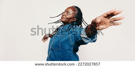 Mature happiness. Carefree woman with dreadlocks standing with her eyes closed and her arms outstretched. Cheerful middle-aged woman wearing a denim jacket and make-up in a studio.