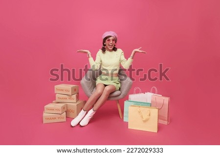 Happy Asian teen woman sitting on sofa with shopping bags and gift box isolated on pink background, Shopper or shopaholic concept.
