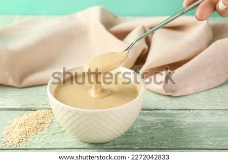 Female hand with bowl and spoon of tasty tahini on color wooden table Royalty-Free Stock Photo #2272042833