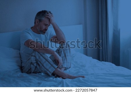 Sleep disorders. Stressed upset thoughtful handsome middle aged man wearing pajamas sitting on bed at night, touching head, awake from bad dream, suffering from nightmares, home interior, copy space Royalty-Free Stock Photo #2272057847