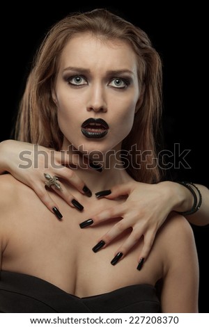 Closeup portrait of a gothic young woman with hands on neck on black background
