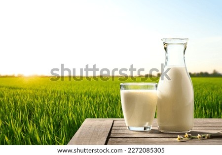 Fresh milk on wooden table with grass field and sunrise background. Royalty-Free Stock Photo #2272085305