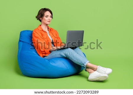 Full length photo of cheerful woman wear denim jacket bean bag typing emails gadget empty space isolated green color background