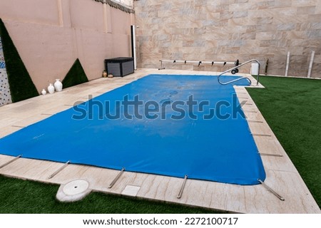 Small pool covered with a blue tarpaulin during the winter season to cover it and prevent dirt and objects from entering the water. Royalty-Free Stock Photo #2272100717