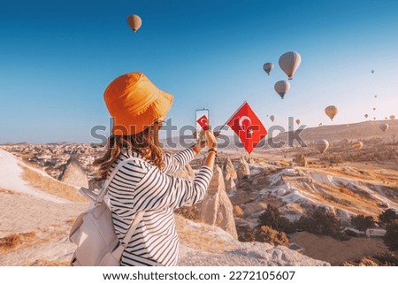 a travel blogger girl takes photos of flying balloons in Cappadocia and the Turkish flag. Social media influencer