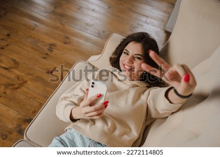 Cheerful young woman sincerely smiles and shows peace sign. Attractive brunette lady.