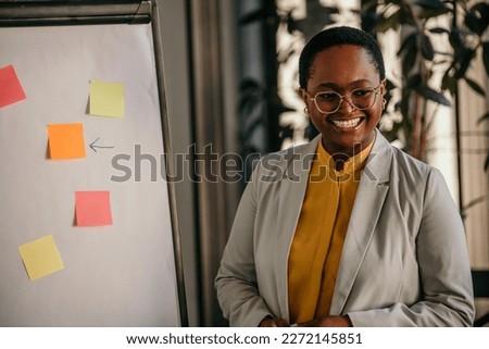 A charming black businesswoman standing next to the whiteboard and giving a business presentation.