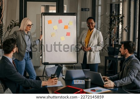 Group of young multiethnic business people working together and preparing new projects at a meeting in the office. Two businesswomen standing with a presentation.