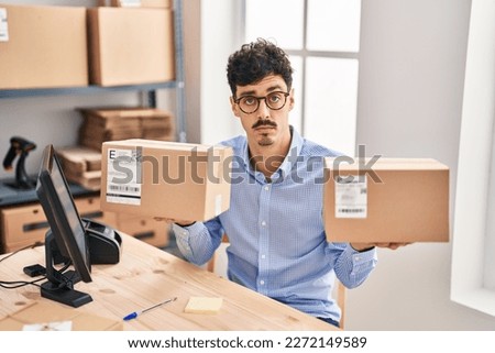 Hispanic man working at small business ecommerce holding packages skeptic and nervous, frowning upset because of problem. negative person. 