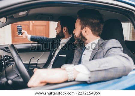 Two elegant contemporary bearded businessmen taking selfie seated in car Royalty-Free Stock Photo #2272154069