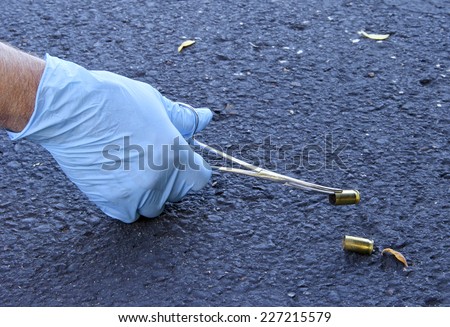 Crime scene investigator is gathering evidence by picking up shell casing using rubber gloves and a forcepts.