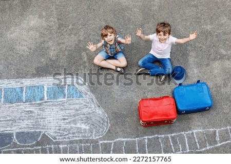 Two little kids boys having fun with train picture drawing with colorful chalks on asphalt. Children having fun with chalk and crayon painting. going on vacations and travel. Friends with suitcases