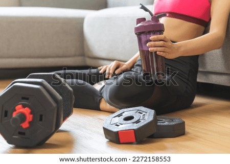 Diet meal replacement for weight loss, asian young woman in sportswear hand holding protein shake bottle, drink supplement for muscle after workout with dumbbell in room at home. Healthy body care. Royalty-Free Stock Photo #2272158553