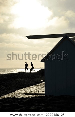 Silhouette of two friends guys playing on the beach near bathhouse at sunset - Boys playing late on the beach - Freedom and youth concept - Vertical editing