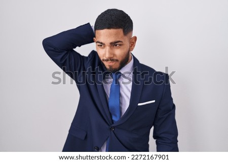 Young hispanic man wearing business suit and tie confuse and wondering about question. uncertain with doubt, thinking with hand on head. pensive concept.  Royalty-Free Stock Photo #2272167901
