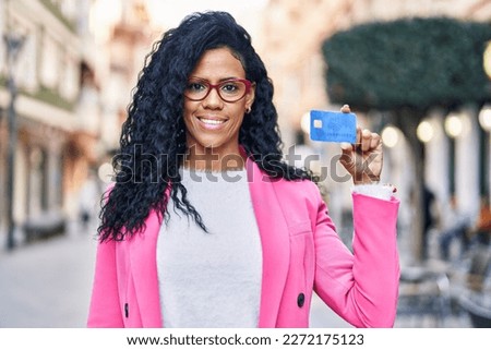 Middle age hispanic woman holding credit card looking positive and happy standing and smiling with a confident smile showing teeth 