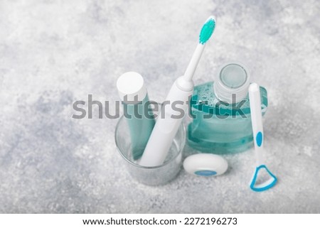Electronic ultrasonic toothbrush, mouthwash, floss, tongue cleaner and toothpaste on blue textured background. Items for dental care and caries prevention in the bathroom. Dentistry concept. Copy spac