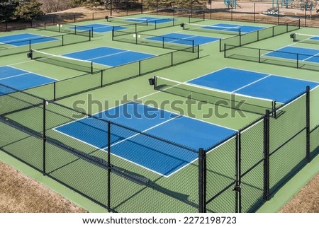 Aerial view of a pickleball complex with blue and green courts beside a playground in a suburban park in early spring. Royalty-Free Stock Photo #2272198723