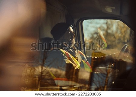 Mid adult driver behind steering wheel of a truck. The view is through the glass. Royalty-Free Stock Photo #2272203085