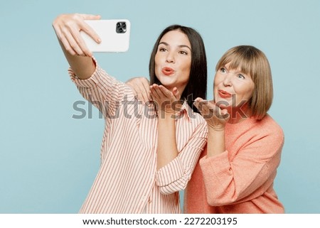 Elder lovely parent mom with young adult daughter two women together wear casual clothes doing selfie shot on mobile cell phone blow air kiss isolated on plain blue cyan background. Family day concept