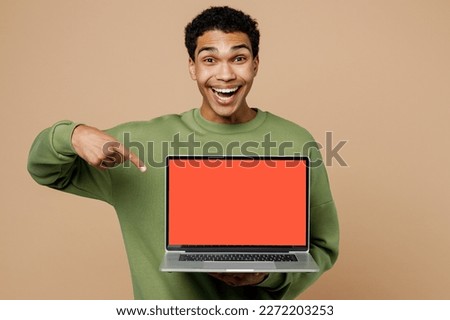Young excited IT man of African American ethnicity wears green sweatshirt hold use work on laptop pc computer with blank screen workspace area isolated on plain pastel light beige background studio