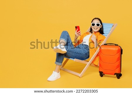 Young woman wear summer clothes sit in deckchair use show mobile cell phone isolated on plain yellow background. Tourist travel abroad in free spare time rest getaway. Air flight trip journey concept Royalty-Free Stock Photo #2272203305
