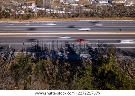 A top down view over traffic on a highway on a sunny day. The sun creates shadows from the trees. There is motion blur from the car's movement and the camera's slow shutter speed.