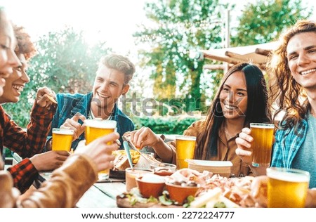 Group of multi ethnic friends having backyard dinner party together -   Millennial people sitting at bar table toasting beer glasses in brewery pub garden - Happy hour, lunch break and youth concept Royalty-Free Stock Photo #2272224777