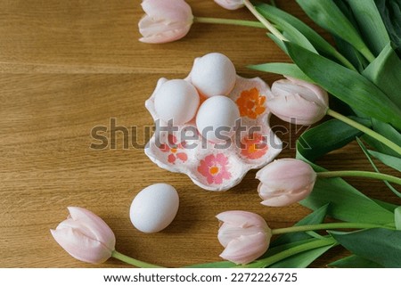 Beautiful tulips and eggs on wooden table. Modern easter decor flat lay. Happy Easter! Stylish handmade egg holder with natural eggs and pink tulips