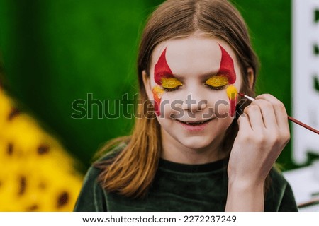 A professional make-up artist, artist paints with a brush on her face with multi-colored paints face painting, drawing, children's makeup for a little girl model. Portrait, art concept, lifestyle. Royalty-Free Stock Photo #2272237249