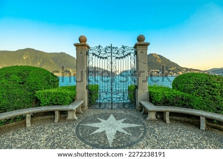 Gate on the Lugano Lake in the public Ciani park of Switzerland. The lakefront of Lugano city in Ticino canton. Park bench with wind rose of stones and with Monte San Salvatore mount. Royalty-Free Stock Photo #2272238191