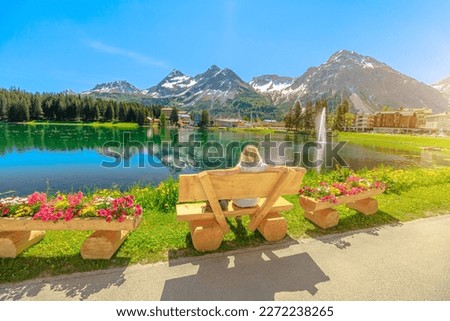 Woman tourist on a park bench of Arosa town at dawn. Touristic resort by Obersee Lake in Switzerland. Arosa lakefront by cable car station to Aroser Weisshorn peak. Plessur Region in Grisons Canton.