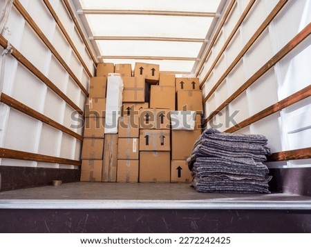 The inside of a removal van, showing fabric blankets stacked and a background of cardboard boxes. Concept for moving home, furniture protection, storage, packing and transportation. Copy space.