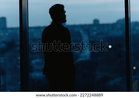 Silhouette of a Business Man looking out of high rise office window at night Royalty-Free Stock Photo #2272248889