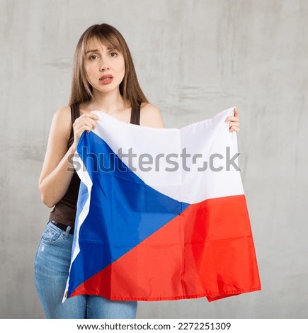 Sad young woman with large flag of Czech Republic posing sorrowfully against light unicoloured background