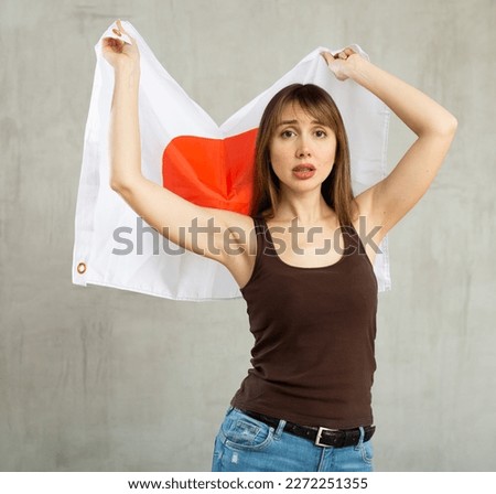 Sad young woman with large flag of Japan posing sorrowfully against light unicoloured background
