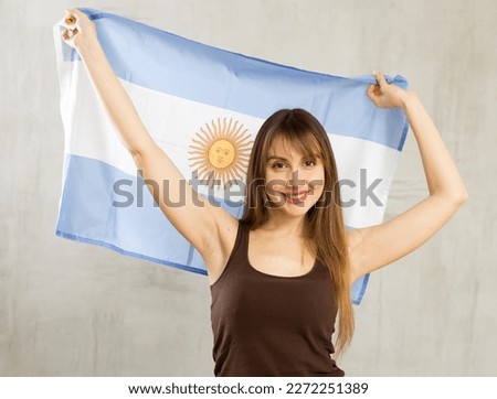 Cheerful young woman holding big Argentina flag in her hands