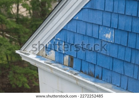 Worn wooden shake siding on an old house in New England. The blue paint is peeling and needs to be repainted. Royalty-Free Stock Photo #2272252485