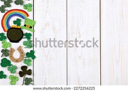 St Patrick's Day concept. Knitted composition of a green hat, a pot of gold, a horseshoe, a rainbow and green shamrocks on a white wooden background. Copy space, flat lay