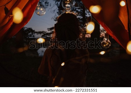 View from the tent. A woman's back against the background of trees and water. Outdoor recreation. The magic is in the picture.