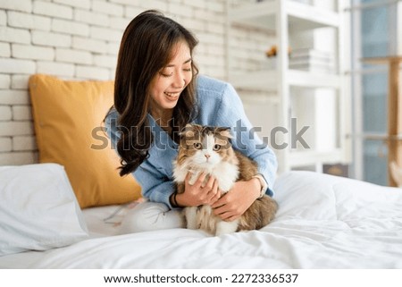 Pretty Asian woman hug cat and sit on bed with happy emotion while cat look at camera with day light. Royalty-Free Stock Photo #2272336537