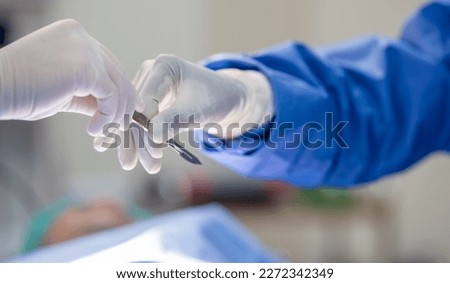 Team of surgery doctor in Operating Room hold hands scalpel surgical blade give to Surgeons During Operation. surgeons assistance in green gown coat give scalpel surgical blade to doctor Royalty-Free Stock Photo #2272342349