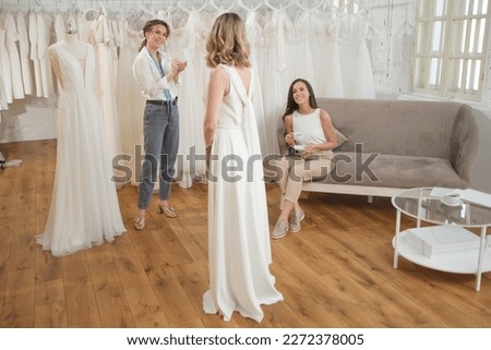 Skillful dress designer fitting wedding gown to woman in her boutique. Woman making adjustments to bridal gown in fashion designer studio. Royalty-Free Stock Photo #2272378005
