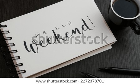 HELLO WEEKEND! black lettering in notebook with cup of espresso and pens on black wooden desk Royalty-Free Stock Photo #2272378701
